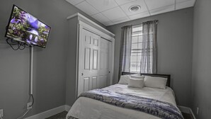 Un dormitorio con cama, televisor en la pared, puerta y ventana con cortinas.