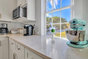 A kitchen with a coffee maker, a kettle, a blender, and a window with a view of the outside.