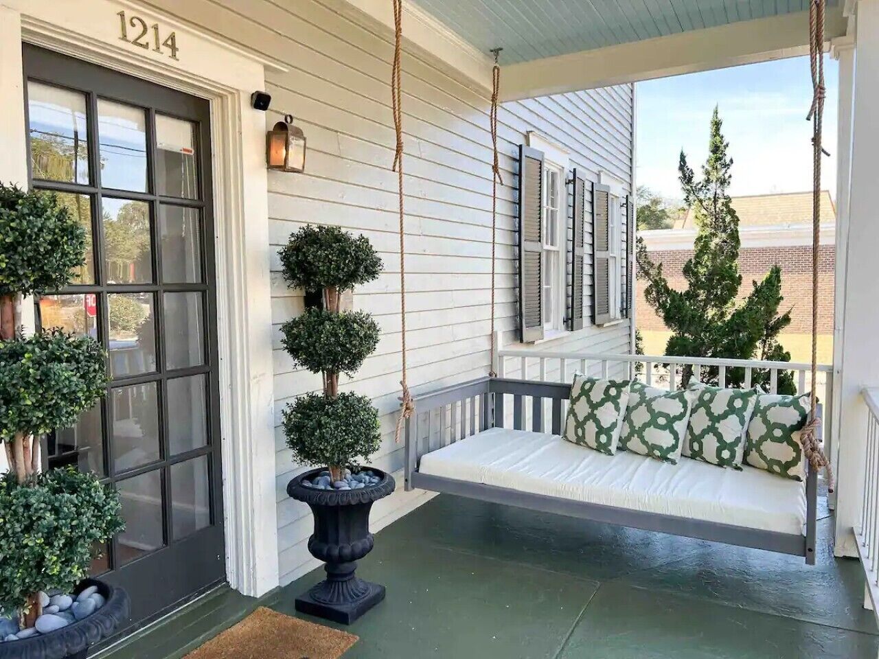 Un porche avec une balançoire, un pot de fleurs et une porte portant le numéro 1214.
