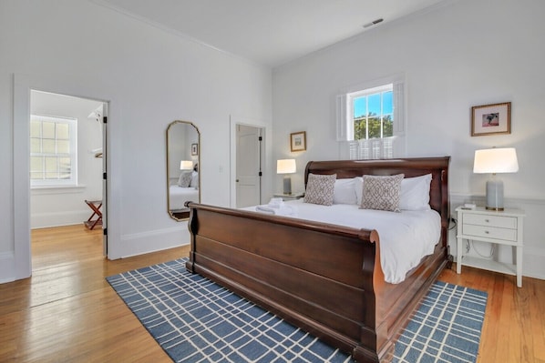 Un dormitorio con cama de madera, una ventana con persianas, un espejo y una mesita de noche con lámpara.