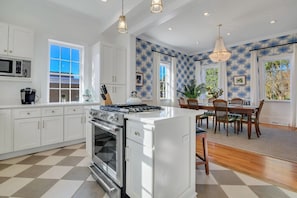 Una cocina moderna con armarios blancos, una isla central y una zona de comedor con mobiliario de madera.
