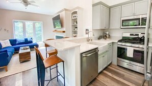 A modern kitchen with a central island, built-in appliances, and a dining area with a blue sofa and bar stools. - New! Cottage Near Squam Lake (Holderness)