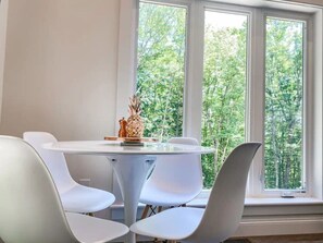 Un coin repas avec une table ronde et des chaises blanches, un ananas en guise de décoration centrale et une vue sur les arbres à travers de grandes fenêtres.