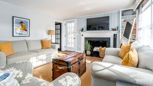 A living room with a fireplace, a sofa, a coffee table, and a television. - New! Chatham Cottage- 1 Mile to Downtown & Beaches (Chatham)