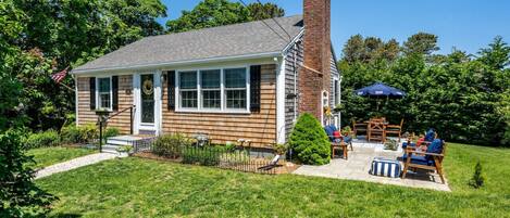 A two-story house with a brick chimney, a front porch, and a patio with outdoor furniture.
