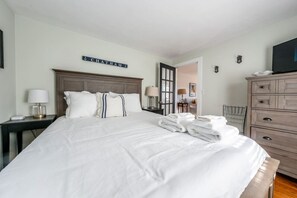 Une chambre d’hôtel avec un grand lit, une table de chevet avec une lampe, une commode et un téléviseur posé sur la commode.