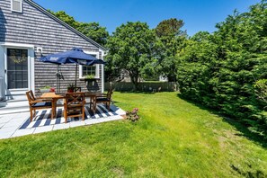 A patio with a table and chairs, a blue umbrella, and a house with a gray roof.