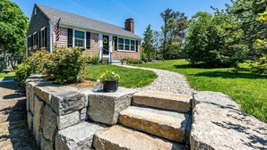 A two-story house with a front porch, a flag, and a well-maintained lawn. - New! Chatham Cottage- 1 Mile to Downtown & Beaches (Chatham)