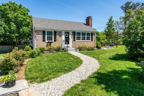 A single-story house with a front porch, a flag, and a well-maintained lawn.