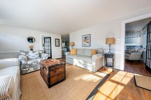 Un salon spacieux comprenant un canapé, un fauteuil à motifs, une commode en bois et une lampe.