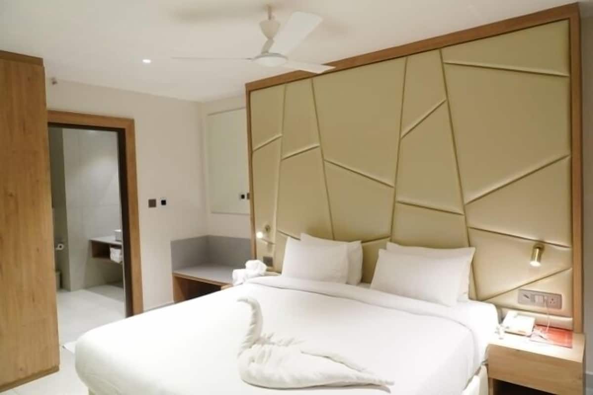Una habitación de hotel moderna con una cama grande, un cabecero con diseños geométricos, una mesita de noche con teléfono y un ventilador de techo.