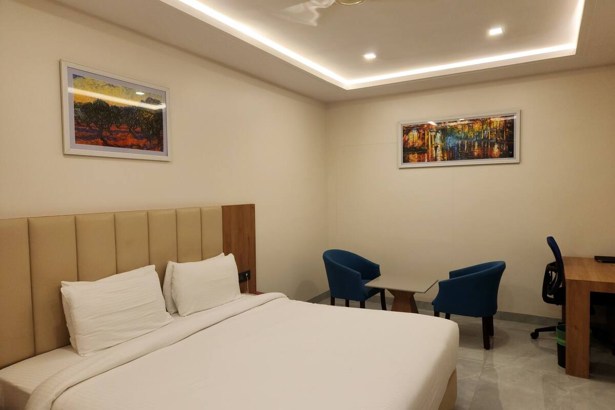 Una habitación de hotel con una cama grande, dos sillas azules, una mesita y dos cuadros enmarcados en las paredes.