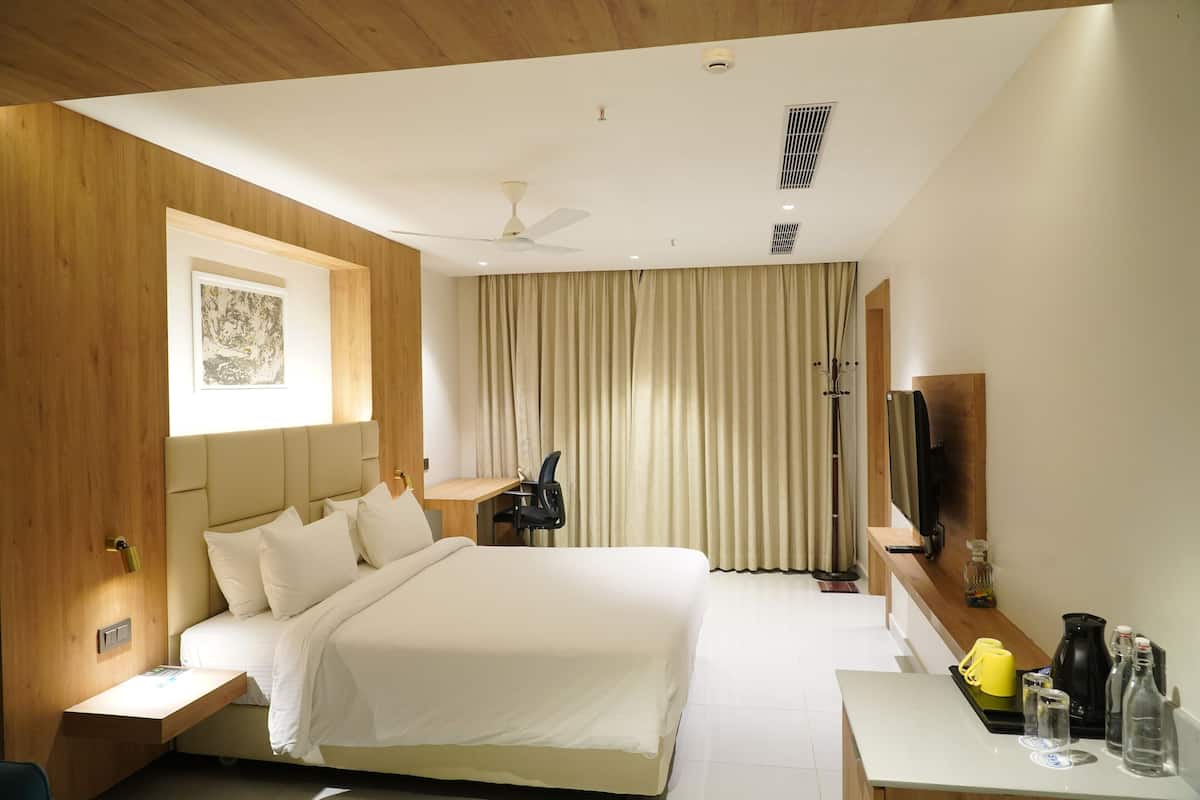 Una habitación de hotel moderna con una cama grande, un escritorio, una silla, un televisor de pantalla plana y una ventana con cortinas.