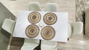 A table with four woven placemats and four white chairs.