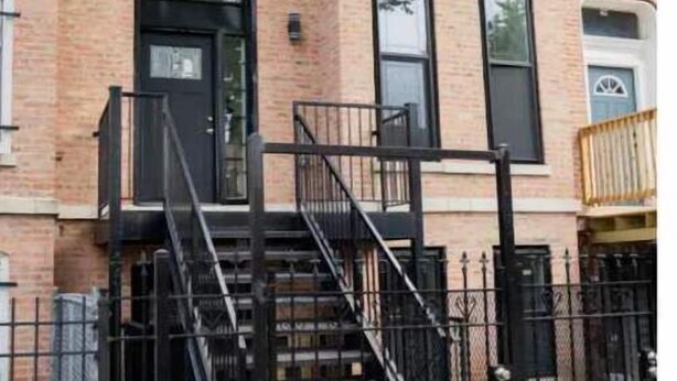 A two-story brick building with a black front door, windows, and a black metal staircase leading to the entrance.