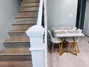 A staircase with wooden steps and white handrails, leading to a dining area with a white table and four chairs. - MODERN HOME: 4BD & 3 FULL BATHS, WFH Setup, Public Transit, 15 Mins to Downtown! (Chicago)