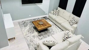 A modern living room with a sofa, a coffee table, and a flat-screen TV mounted on the wall.