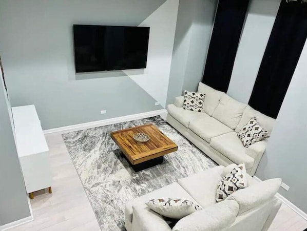A modern living room with a sofa, a coffee table, and a flat-screen TV mounted on the wall. - MODERN HOME: 4BD & 3 FULL BATHS, WFH Setup, Public Transit, 15 Mins to Downtown! (Chicago)
