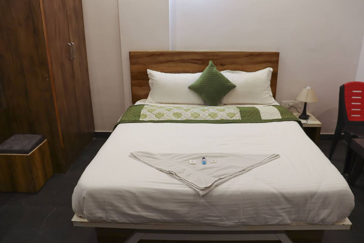 Ein ordentlich bezogenes Bett mit einem hölzernen Kopfteil, einem grünen Kopfkissen und einer weißen Decke.