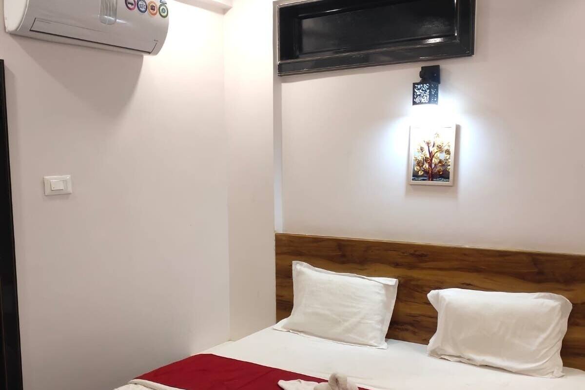 Ein Hotelzimmer mit Bett, Deckenventilator, Klimaanlage, flachbildfernseher an der Wand und einem kleinen gerahmten Bild über dem Fernseher.