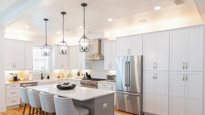 Una cocina moderna con armarios blancos, electrodomésticos de acero inoxidable y una isla central con taburetes de bar.