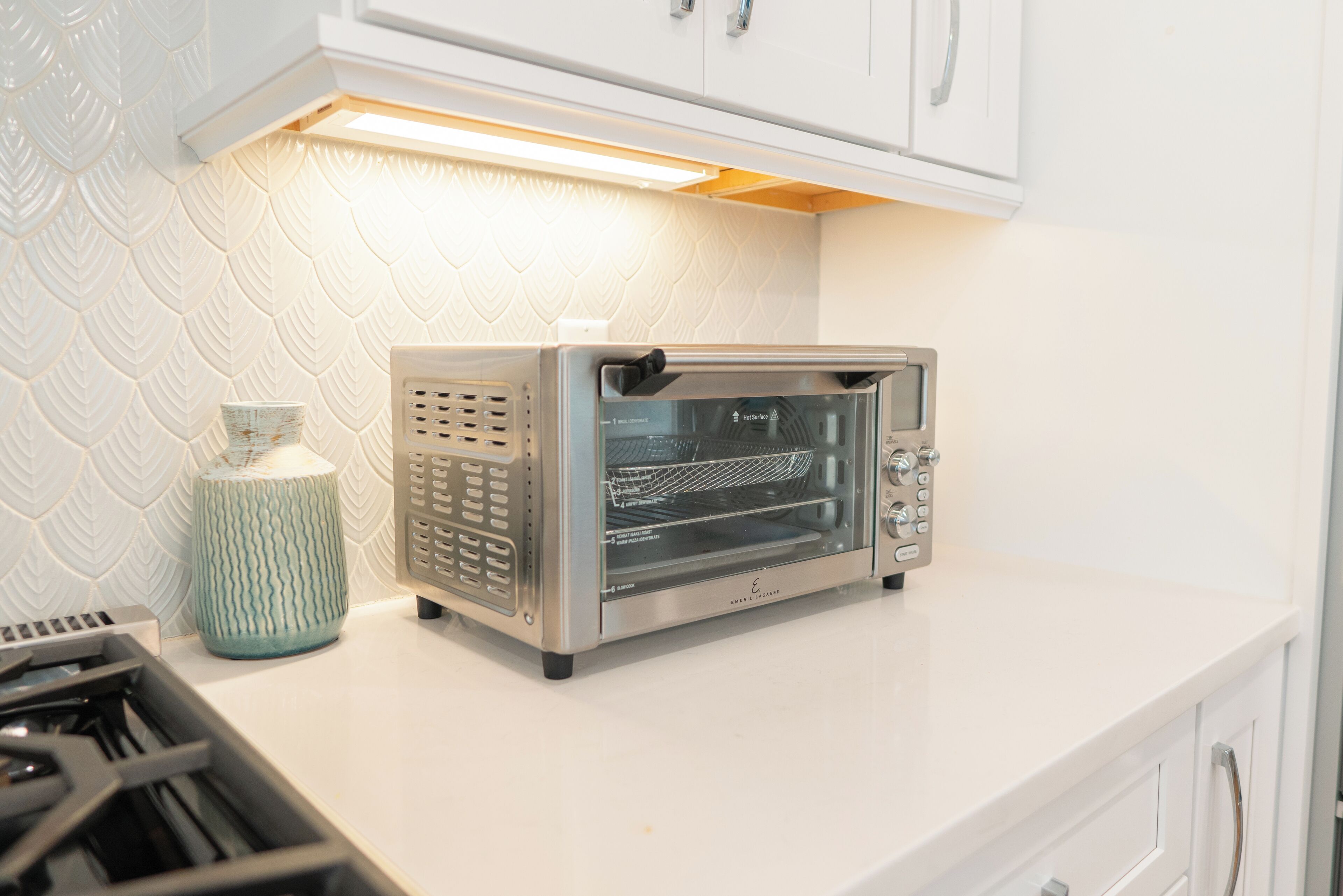 A kitchen with a built-in toaster oven, a kettle, and a stove.