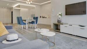 Un salon moderne avec un canapé gris, deux petites tables rondes blanches et un coin repas avec des chaises bleues.