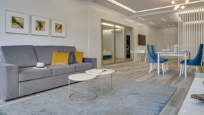 Un salon moderne avec un canapé gris, une petite table ronde et un coin repas avec des chaises bleues.