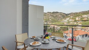 Un balcon avec une table ronde préparée pour le petit-déjeuner, avec des croissants, des fruits et des tasses.