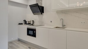 Une cuisine moderne avec des meubles blancs, un four encastré, une machine à café et un évier en acier inoxydable.
