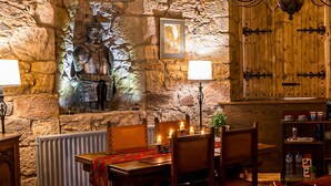 Una habitación de paredes de piedra con una estatua de un caballero medieval, una puerta de madera y una mesa dispuesta para cenar con velas.
