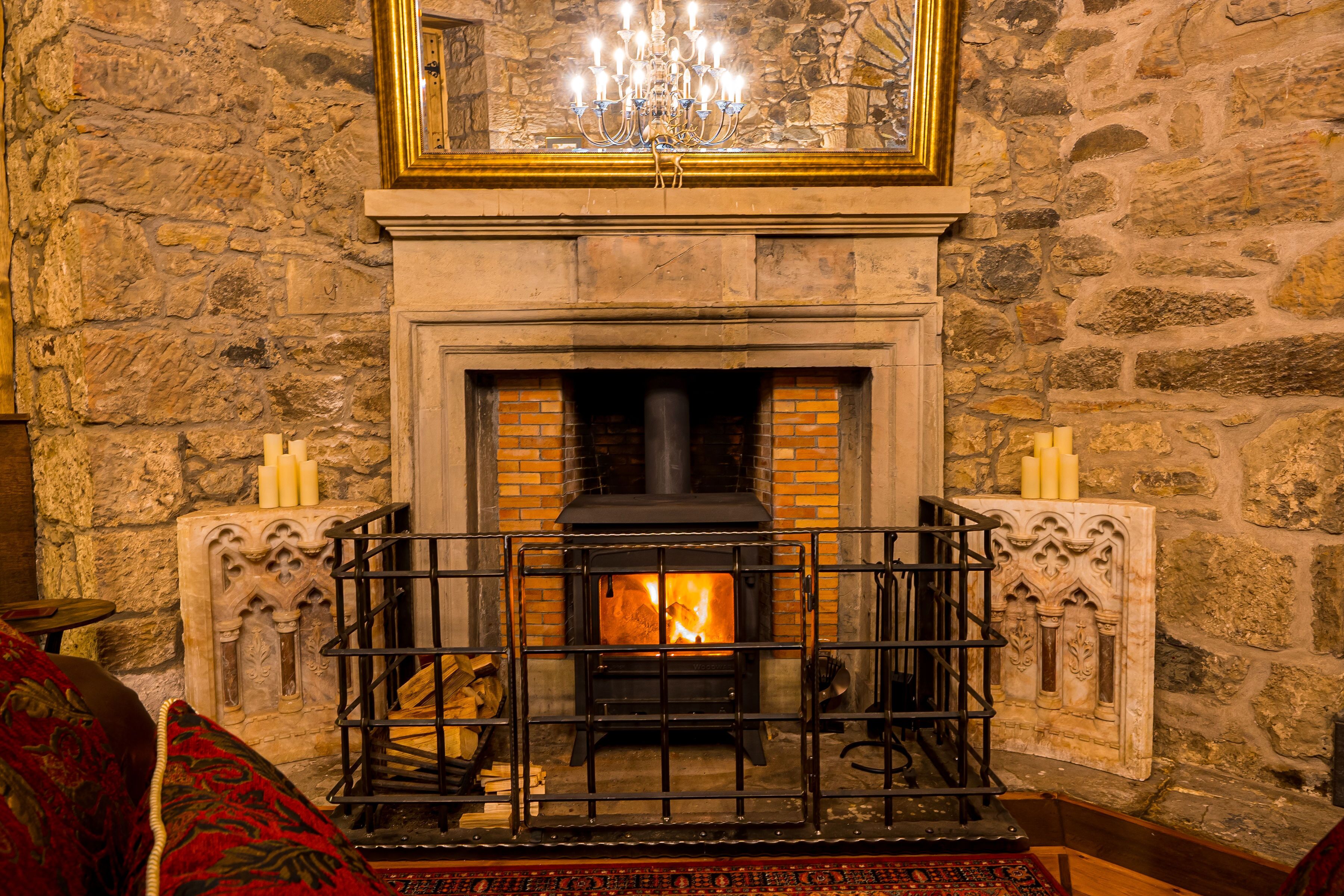 A stone fireplace with a black wood-burning stove, a chandelier above, and candles on either side.
