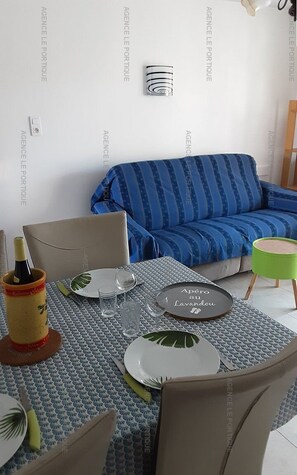 A dining area with a table set for two, a sofa, and a small green stool.