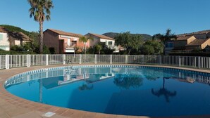 A swimming pool surrounded by a white fence, with houses and palm trees in the background.
