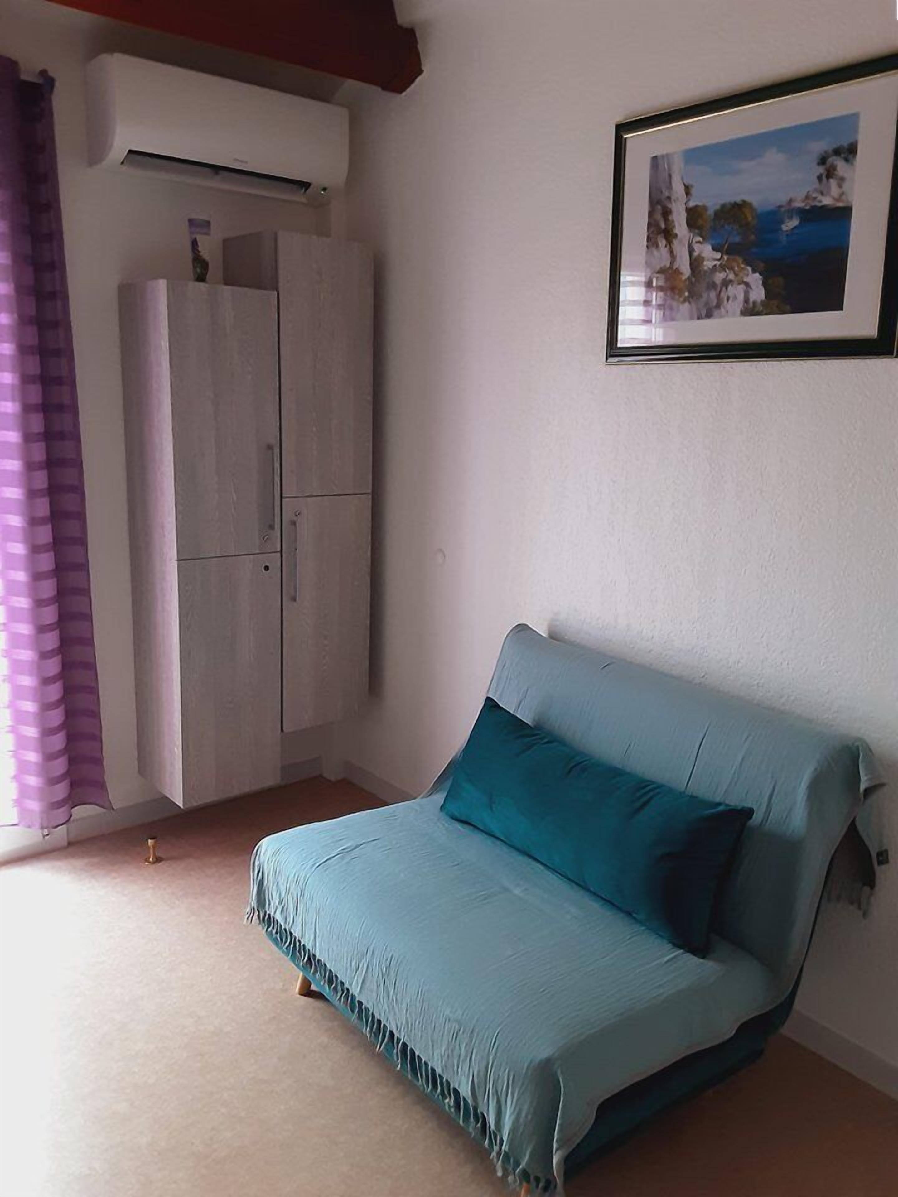 A bedroom with a bed, a wardrobe, an air conditioning unit, and a framed picture on the wall.