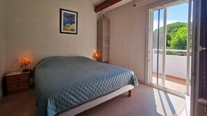 A bedroom with a bed, a nightstand, a lamp, a framed picture on the wall, and a sliding glass door leading to a balcony.