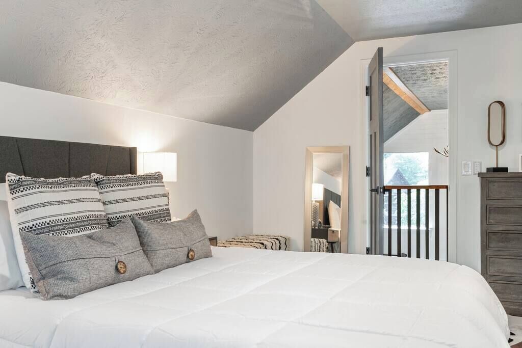 Une chambre à coucher avec un grand lit, une tête de lit et une table de chevet. Une porte donne sur un balcon.