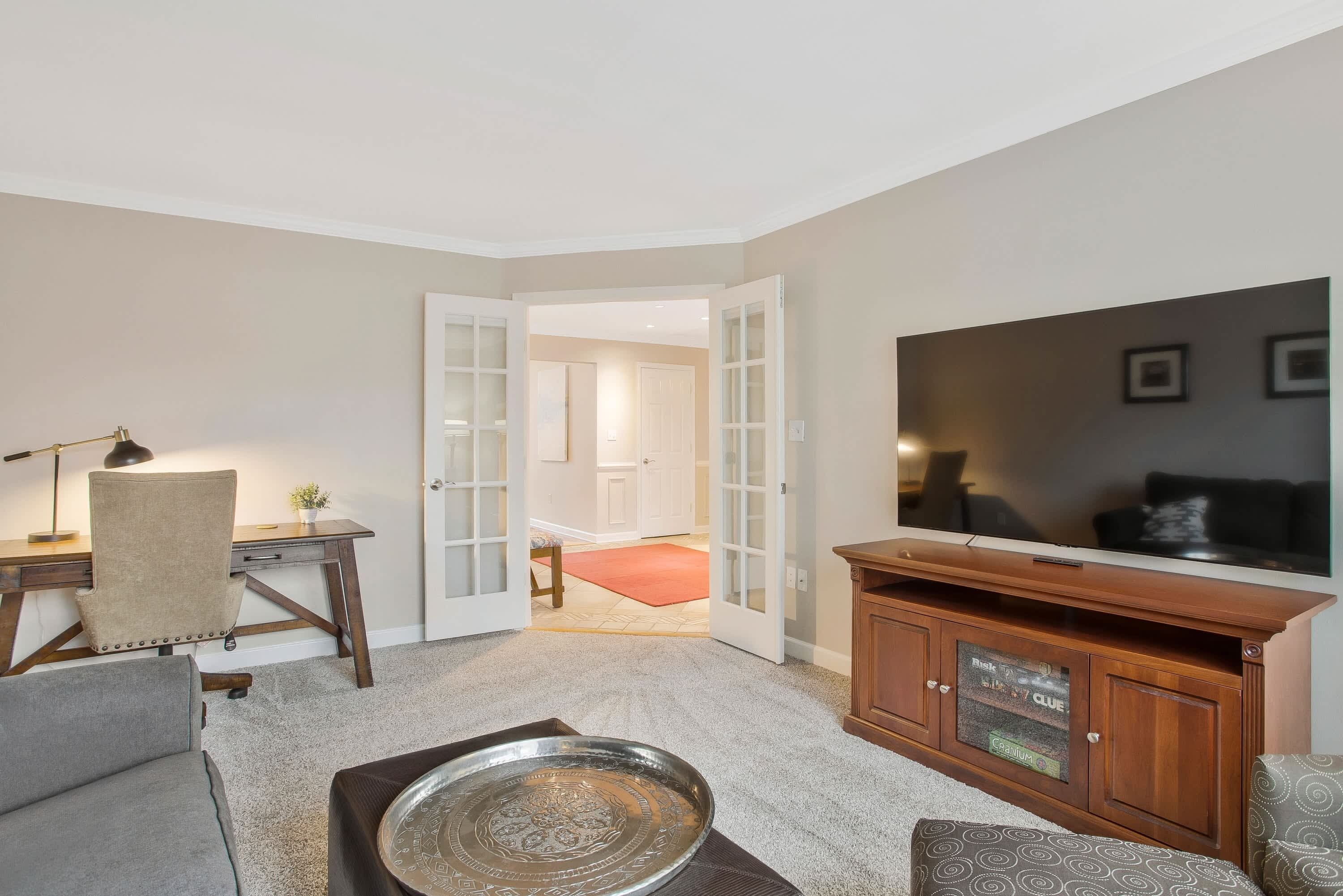 A living room with a desk, a television, a cabinet, and a door leading to another room.