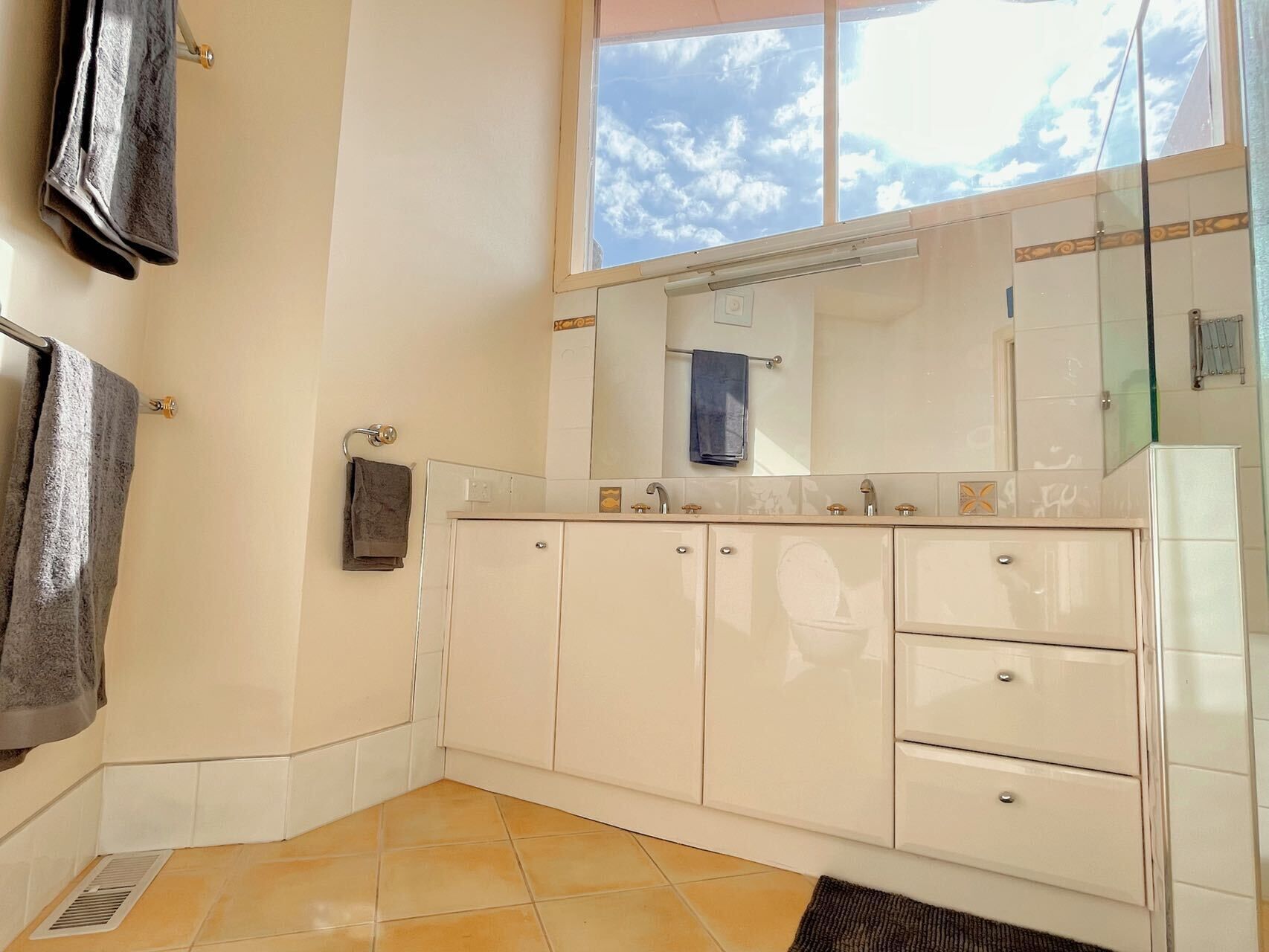 A bathroom with a large window, a mirror, a sink, and a towel rack.