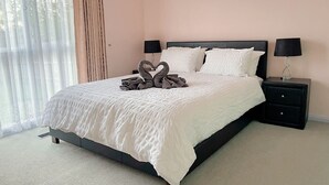 A neatly made bed with a heart-shaped towel arrangement, two bedside tables with lamps, and a window with sheer curtains. - The peaceful retreat in a tranquil court (Mulgrave)