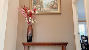 A hallway with a framed painting of a street scene, a vase with flowers, and a wooden console table. - The peaceful retreat in a tranquil court (Mulgrave)
