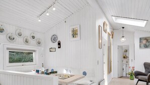 Un salon moderne aux tons clairs, avec un espace repas, doté d’une grande fenêtre, d’une cheminée et d’un coin salon confortable.