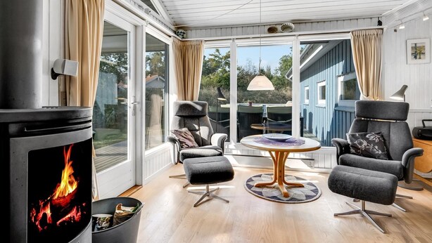 Une pièce chaleureuse avec une cheminée, des fauteuils confortables et de grandes fenêtres donnant sur l’extérieur.