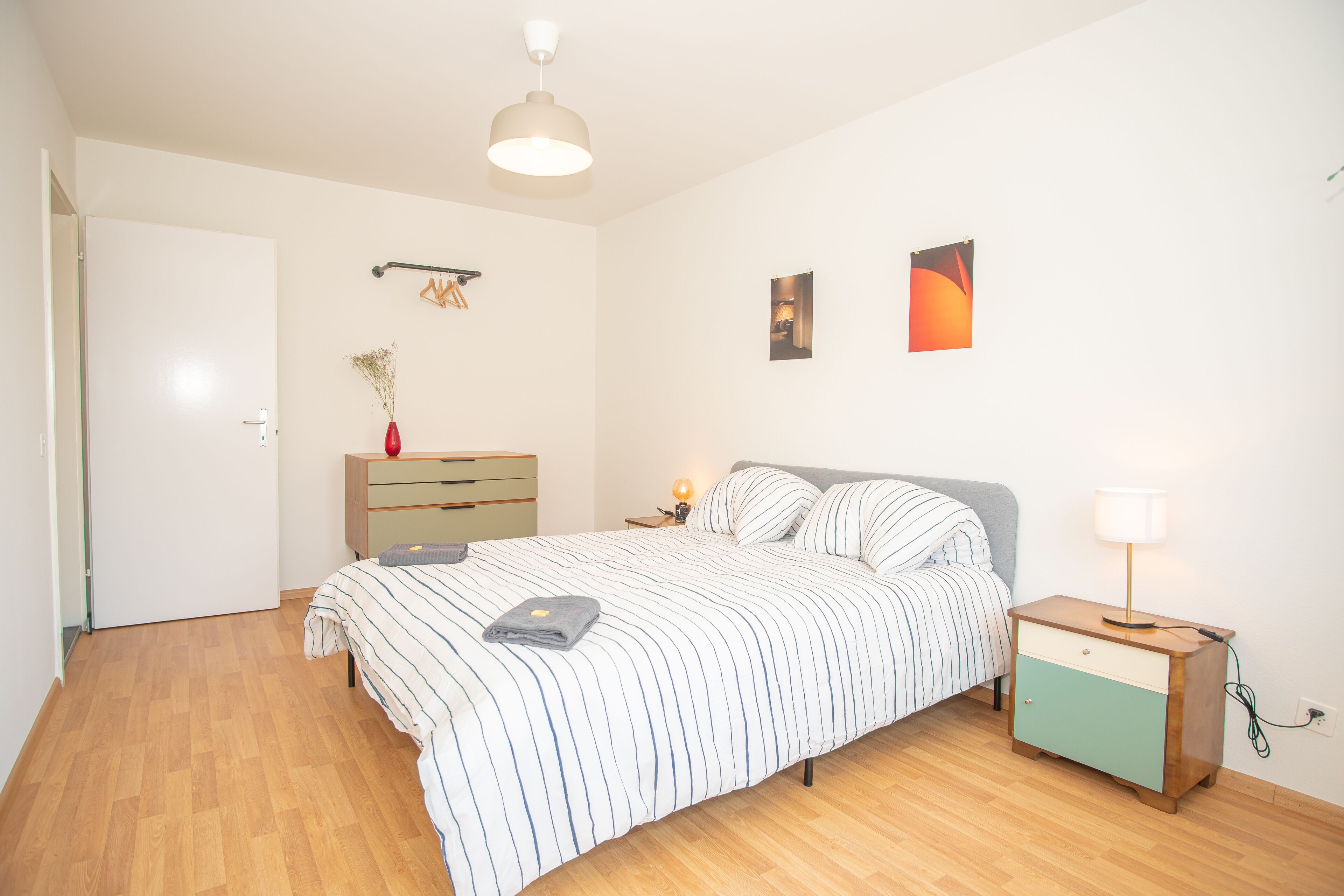 A bedroom with a bed, bedside table, lamp, dresser, and wall art.