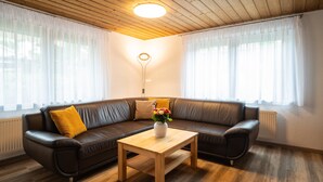 A modern living room with a brown leather sofa, a wooden coffee table, and a vase with flowers. - Ferienwohnung Simssee 60 qm (Rimsting)