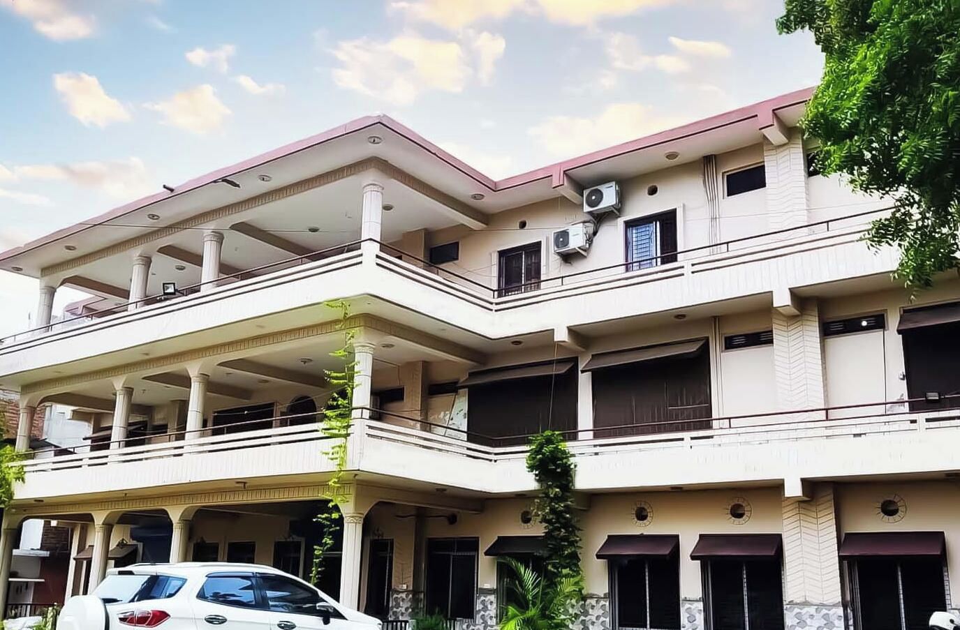 A multi-story building with balconies, air conditioning units, and a car parked in front.
