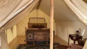 Um quarto com tenda, uma cama de madeira, uma mesinha com um candeeiro, um tapete estampado e uma cadeira.