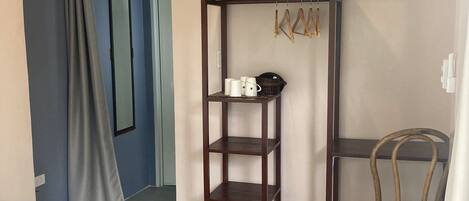 A room with a bed, a wooden wardrobe, a wicker chair, and a door leading to another room.