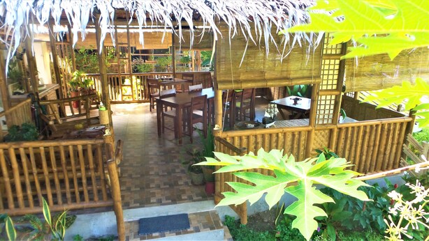 A bamboo structure with a thatched roof, wooden furniture, and potted plants. - The Lazy Tiki (Buenavista)