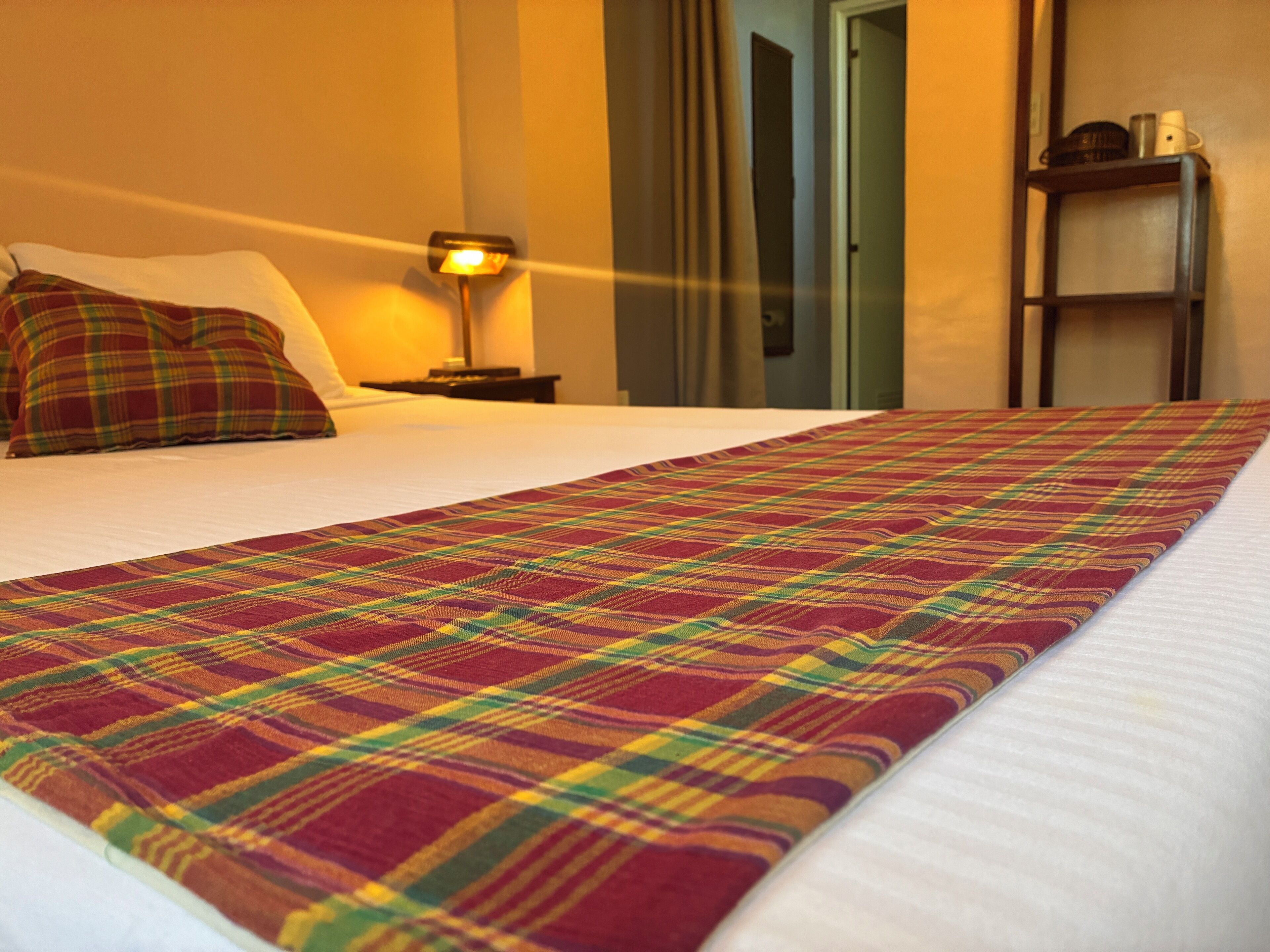 Een hotelkamer met een opgemaakt bed, een bedlampje en een plank met spullen erop.